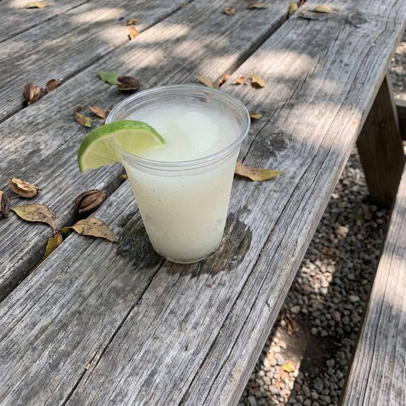 A frozen margarita with lime on a weathered picnic table in pecan shade.
